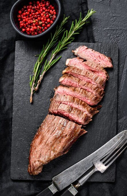 Grill Restaurant Beef Menu - Flank Steak on a black stone Board. Black background. Top view